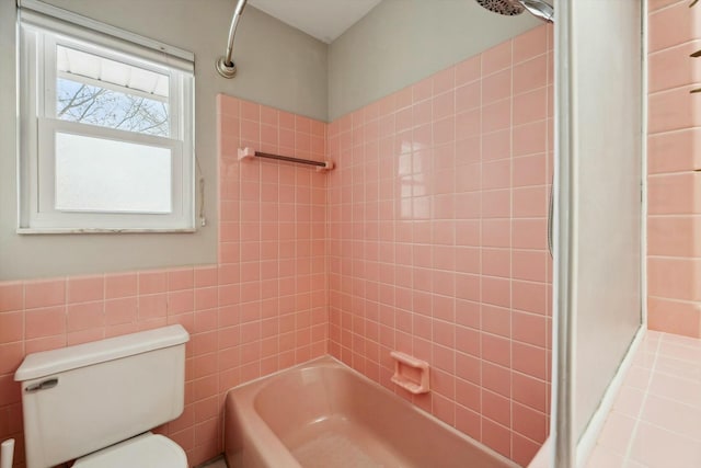 bathroom featuring toilet, tiled shower / bath combo, and tile walls