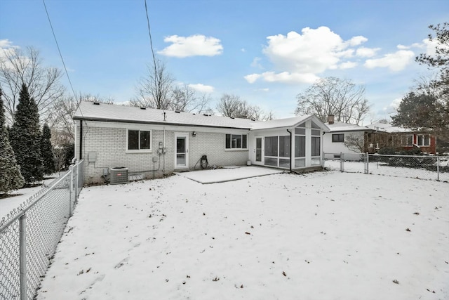 snow covered back of property featuring a sunroom and central air condition unit