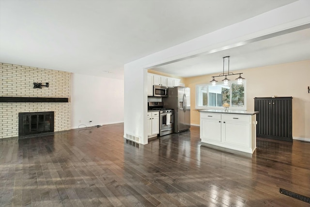 kitchen with dark wood-type flooring, white cabinetry, a brick fireplace, pendant lighting, and stainless steel appliances