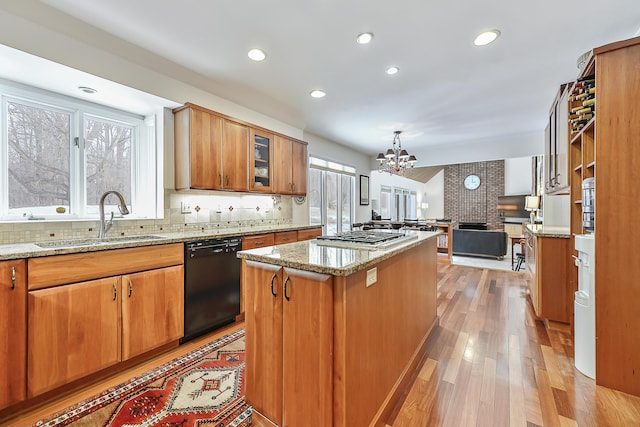 kitchen featuring light stone counters, black dishwasher, a center island, and sink