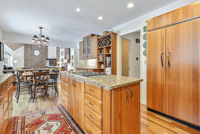 kitchen featuring a kitchen island, hanging light fixtures, stainless steel gas cooktop, light stone counters, and light hardwood / wood-style flooring