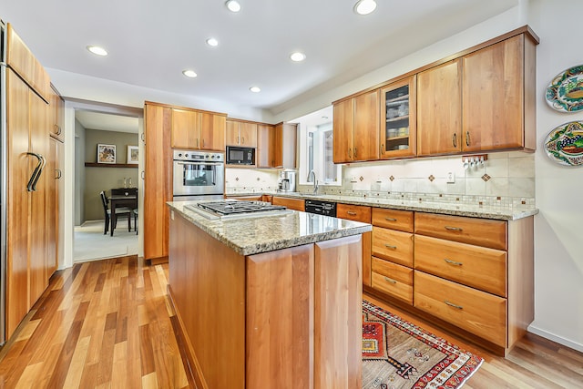 kitchen featuring a kitchen island, light hardwood / wood-style flooring, light stone counters, and black appliances