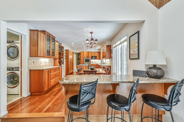 kitchen with an inviting chandelier, backsplash, light stone counters, stacked washer / drying machine, and kitchen peninsula