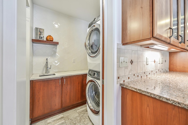 laundry room featuring sink, cabinets, and stacked washer / dryer