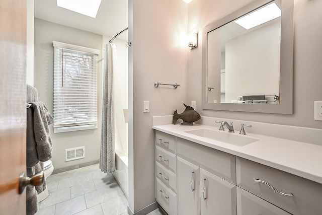 full bathroom with shower / bathtub combination with curtain, a skylight, vanity, tile patterned floors, and toilet