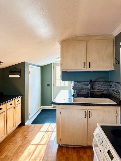 kitchen with electric stove, sink, hardwood / wood-style flooring, light brown cabinetry, and vaulted ceiling