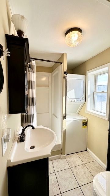 full bathroom with stacked washer and dryer, vanity, tile patterned floors, toilet, and shower / bath combo with shower curtain