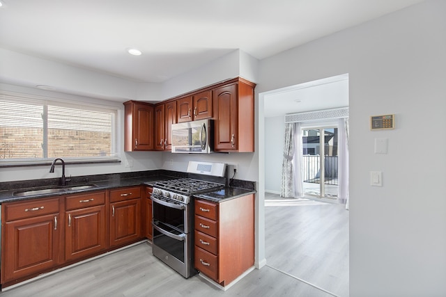 kitchen featuring sink, light hardwood / wood-style flooring, dark stone counters, and appliances with stainless steel finishes