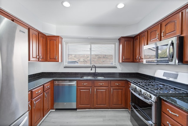 kitchen with appliances with stainless steel finishes, sink, dark stone countertops, and light hardwood / wood-style floors