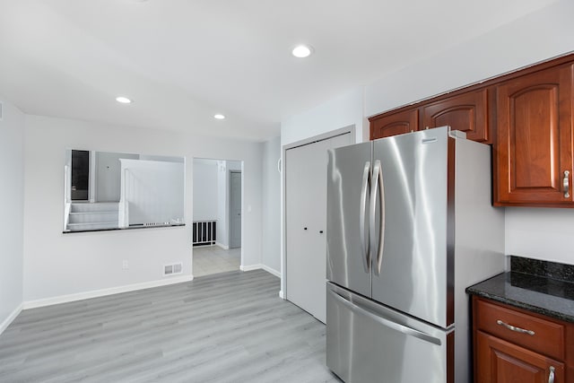 kitchen featuring stainless steel fridge, light hardwood / wood-style flooring, and dark stone countertops