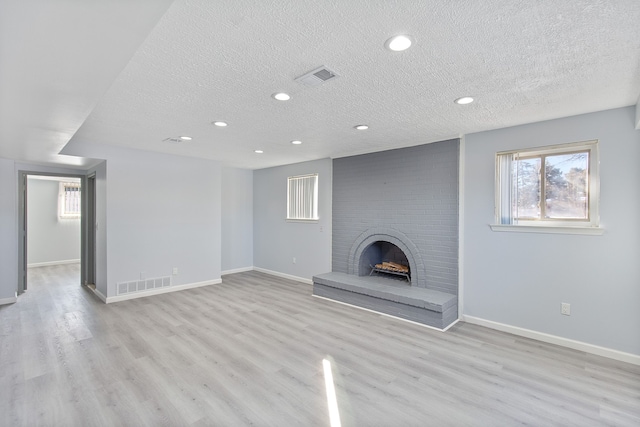 unfurnished living room featuring a brick fireplace, a textured ceiling, and light wood-type flooring