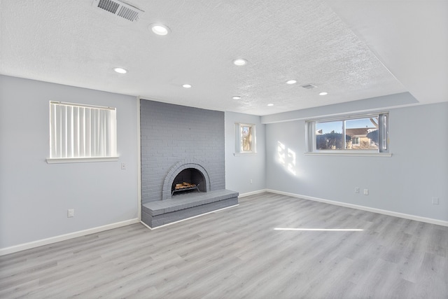 unfurnished living room with a fireplace, light hardwood / wood-style floors, and a textured ceiling