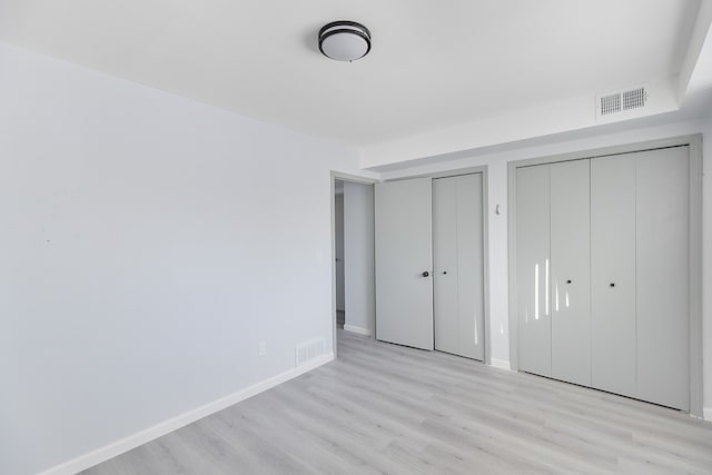 unfurnished bedroom featuring light hardwood / wood-style flooring and multiple closets