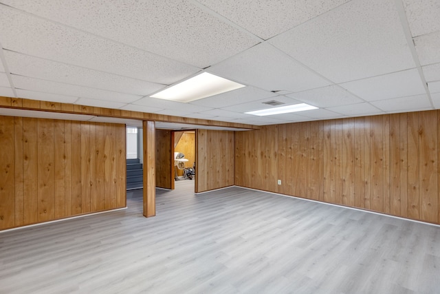 basement featuring a drop ceiling, hardwood / wood-style flooring, and wooden walls