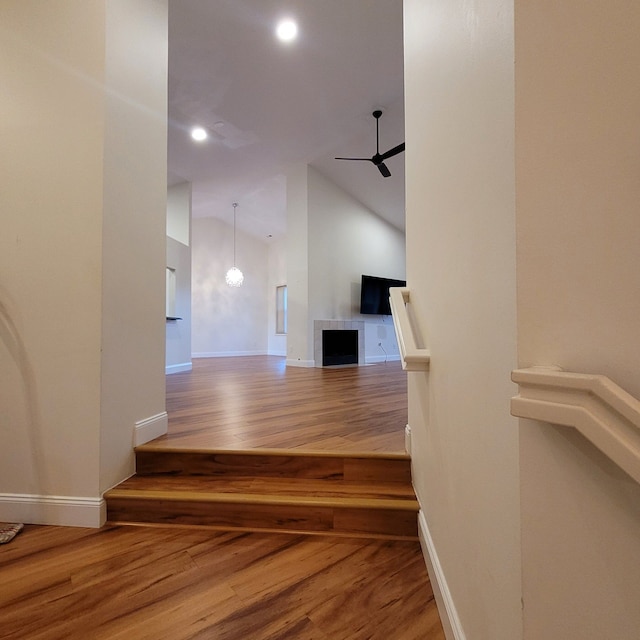 stairway with a tiled fireplace, hardwood / wood-style flooring, high vaulted ceiling, and ceiling fan