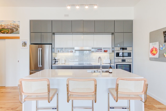 kitchen with sink, a breakfast bar area, gray cabinets, appliances with stainless steel finishes, and a center island with sink