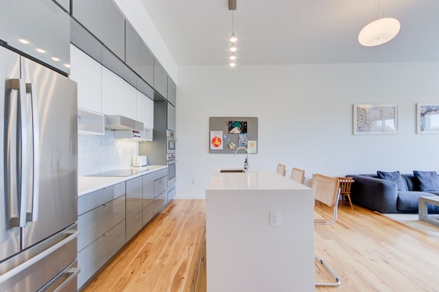 kitchen with sink, appliances with stainless steel finishes, a kitchen island with sink, tasteful backsplash, and decorative light fixtures