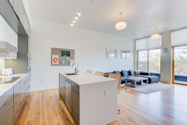 kitchen with decorative light fixtures, sink, white cabinets, a kitchen island with sink, and light hardwood / wood-style floors