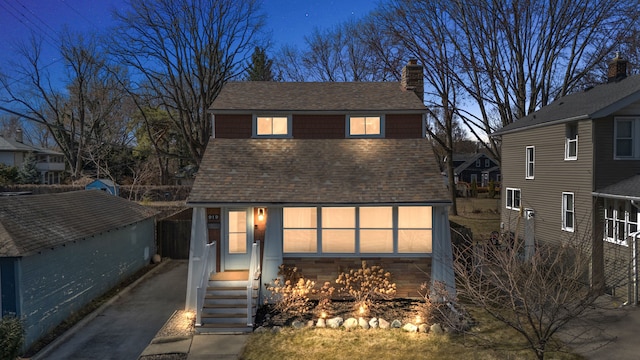 view of front facade featuring an outbuilding, a chimney, and a shingled roof