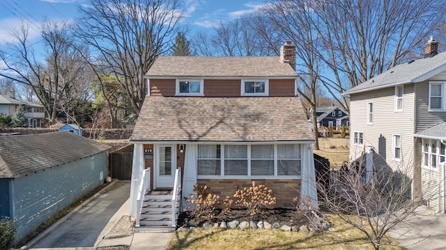 view of front of property with stone siding, a chimney, fence, and a shingled roof