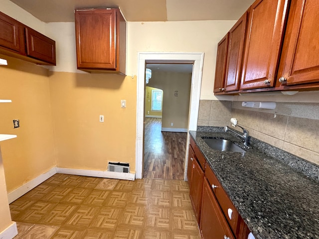 kitchen with light parquet flooring, dark stone counters, sink, and decorative backsplash