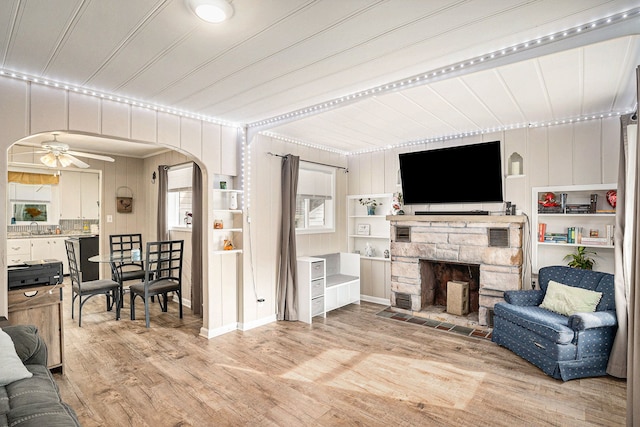 living room with ceiling fan, wooden walls, ornamental molding, light hardwood / wood-style floors, and a stone fireplace