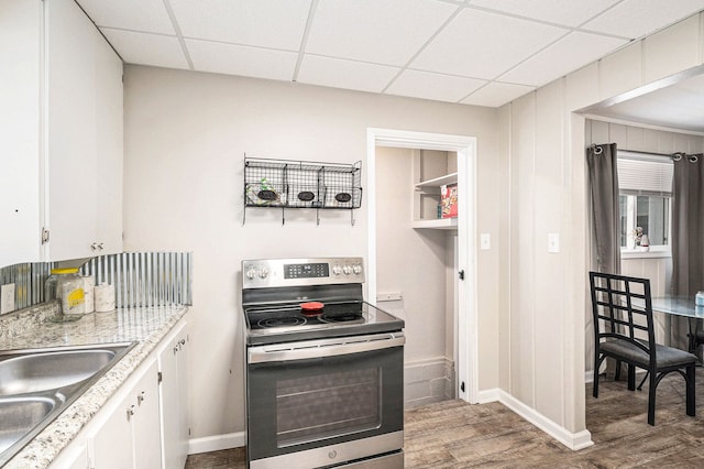 kitchen with sink, white cabinetry, stainless steel electric range oven, hardwood / wood-style flooring, and a drop ceiling