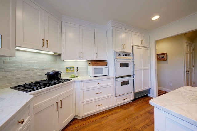 kitchen with hardwood / wood-style flooring, white appliances, light stone countertops, decorative backsplash, and white cabinets