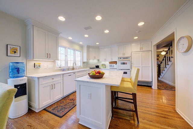 kitchen with sink, white appliances, light hardwood / wood-style flooring, white cabinetry, and a kitchen island