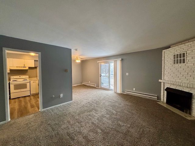 unfurnished living room featuring a brick fireplace, carpet floors, and baseboard heating