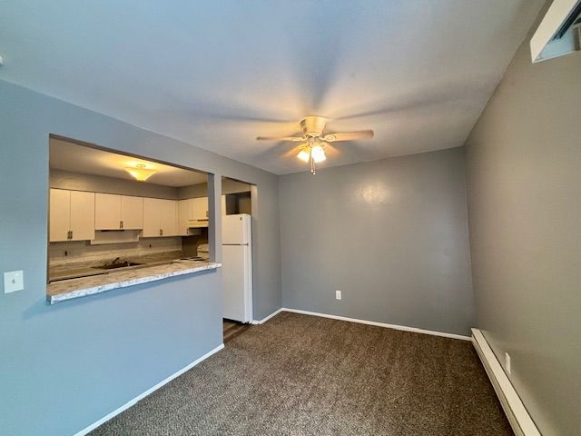 kitchen featuring white cabinetry, white refrigerator, baseboard heating, dark carpet, and ceiling fan