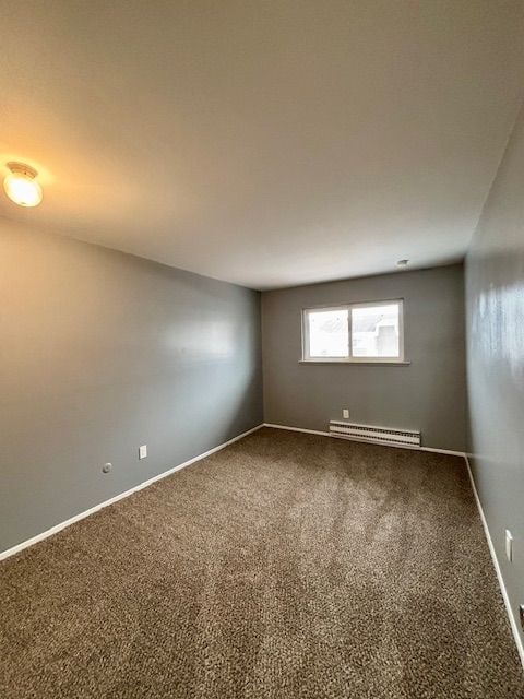 spare room with carpet floors and a baseboard heating unit