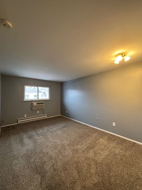 unfurnished room with carpet floors, a wall unit AC, and a baseboard heating unit