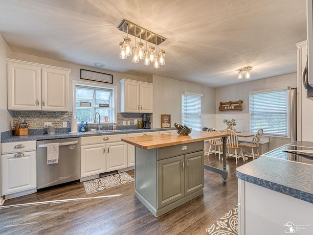 kitchen featuring wooden counters, white cabinetry, a kitchen island, decorative light fixtures, and stainless steel dishwasher