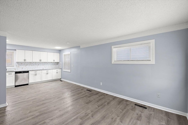 kitchen featuring dishwasher, white cabinets, backsplash, light hardwood / wood-style floors, and a textured ceiling