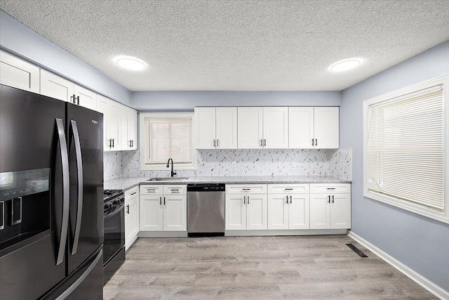 kitchen with white cabinetry, sink, backsplash, light stone counters, and black appliances