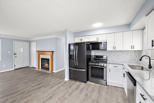 kitchen with sink, white cabinetry, stainless steel appliances, tasteful backsplash, and light stone countertops