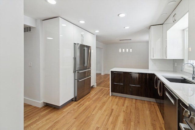 kitchen with sink, white cabinetry, stainless steel appliances, dark brown cabinetry, and light hardwood / wood-style floors