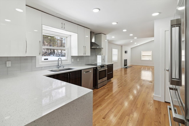 kitchen featuring wall chimney exhaust hood, sink, tasteful backsplash, appliances with stainless steel finishes, and white cabinets