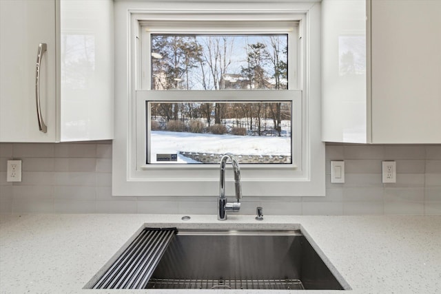 room details with white cabinetry, sink, light stone counters, and decorative backsplash