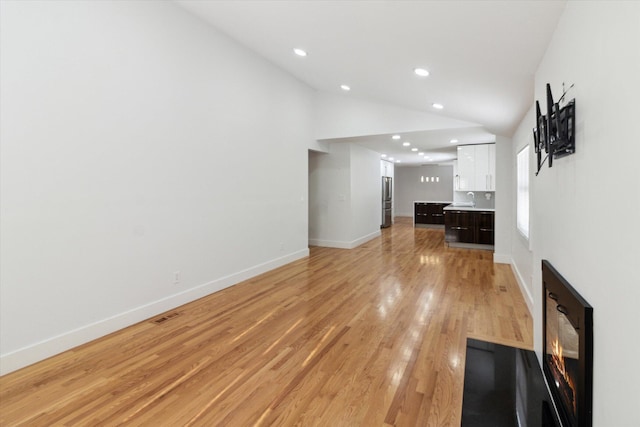 unfurnished living room with sink, vaulted ceiling, and light hardwood / wood-style flooring