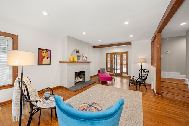 living room featuring beamed ceiling, a brick fireplace, light hardwood / wood-style floors, and french doors