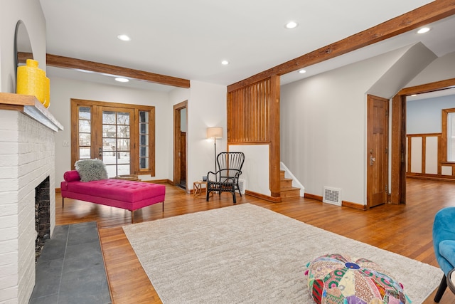 sitting room with beamed ceiling, a fireplace, and hardwood / wood-style floors