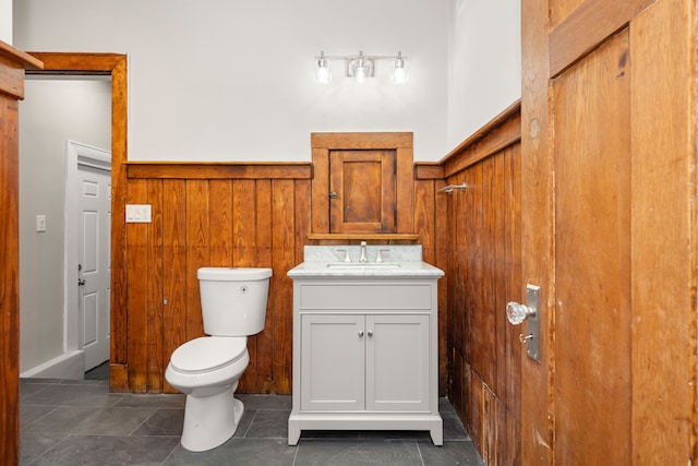 bathroom with vanity, tile patterned floors, toilet, and wood walls