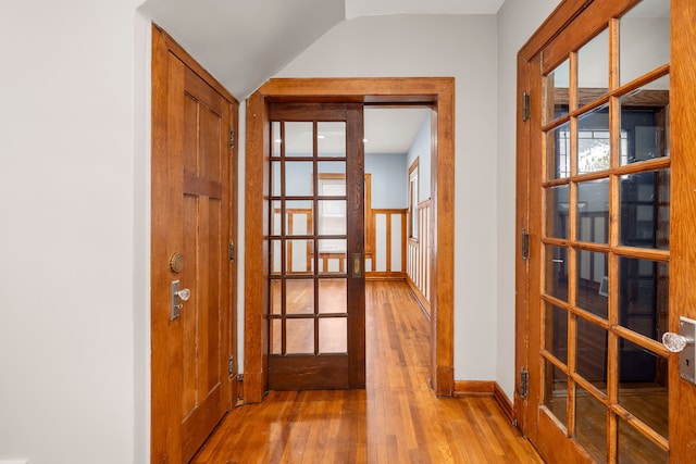 corridor with french doors, vaulted ceiling, and light hardwood / wood-style floors