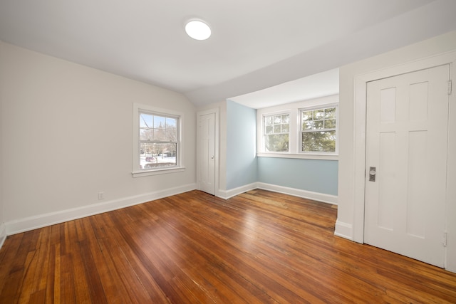 spare room featuring lofted ceiling, hardwood / wood-style flooring, and a healthy amount of sunlight