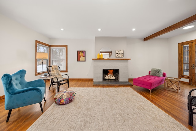 living room with a brick fireplace, beam ceiling, and light wood-type flooring