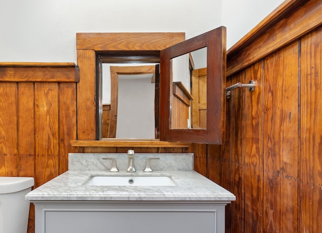 bathroom featuring wooden walls, vanity, and toilet