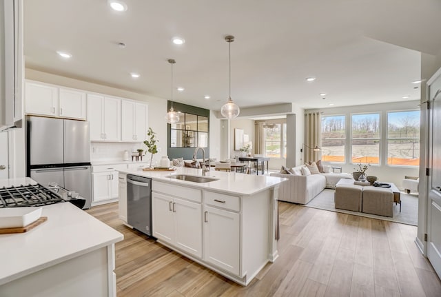 kitchen featuring stainless steel appliances, a sink, white cabinets, open floor plan, and light countertops