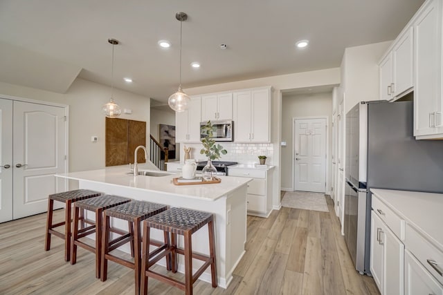 kitchen with a center island with sink, stainless steel appliances, light countertops, white cabinetry, and a sink